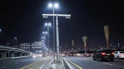 Illuminated LED streetlights line a multi-lane highway in Abu Dhabi at night with traffic and palm trees.