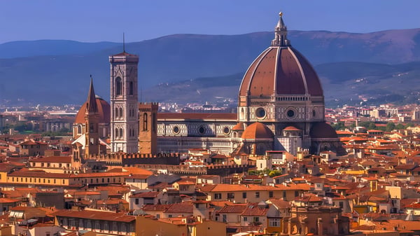 Panoramic view of the Florence city skyline featuring the Duomo and Giotto's Bell Tower against a mountain backdrop.