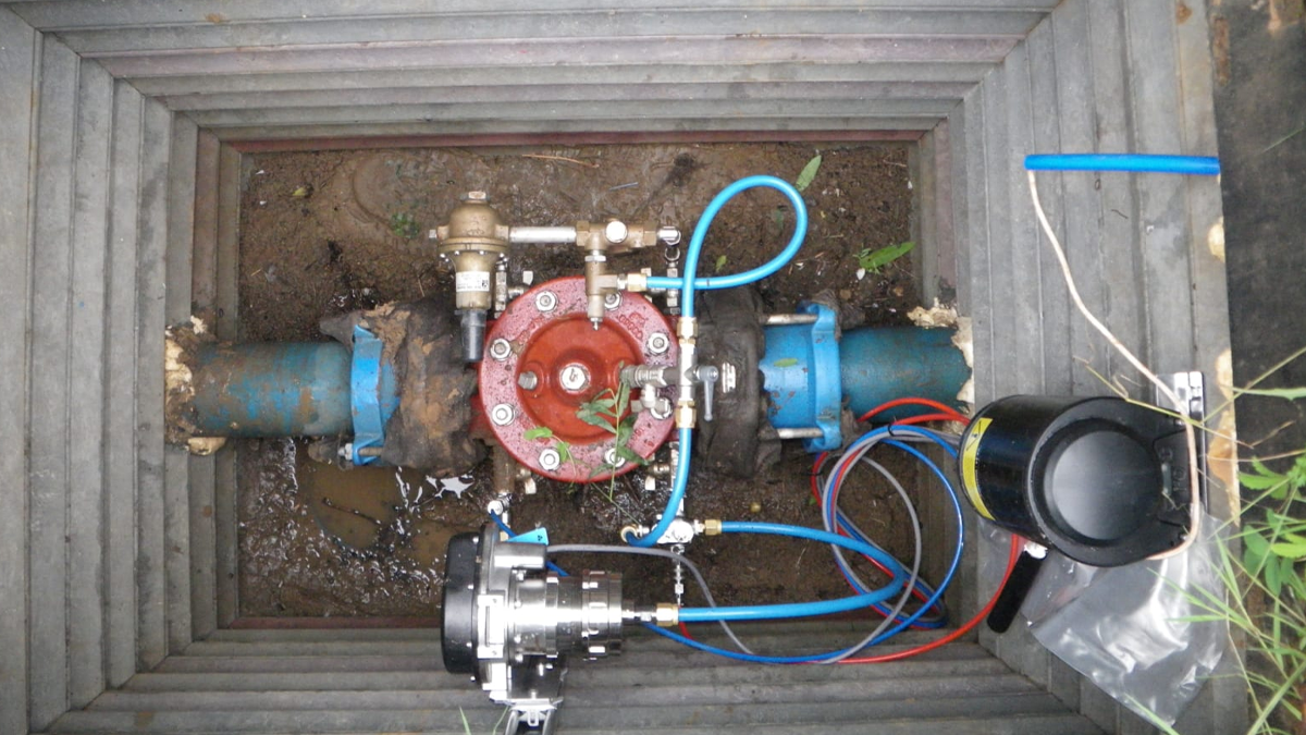 An underground water pipe installation with a red control valve, blue tubing, and electronic monitoring equipment