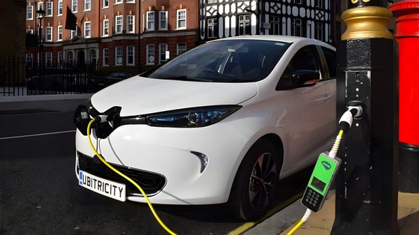 White Renault Zoe with Ubitricity branding charging from a London street lamp using a green Ubitricity SmartCable.