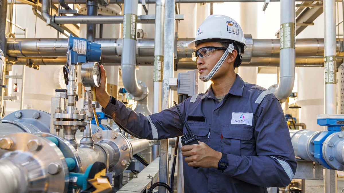 A Gradiant engineer in a hard hat and safety glasses inspects a pressure gauge at an industrial water treatment facility.