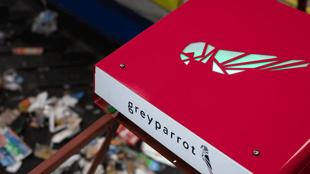 Red Greyparrot monitoring unit with an illuminated logo installed over a conveyor belt of waste.