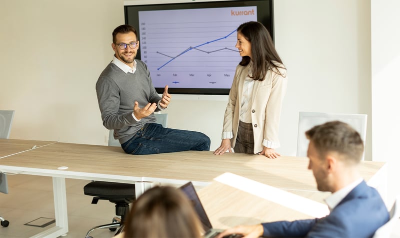 A man and woman sit at a table in front of a large screen, discussing smart city and utility growth strategy.