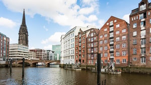 Historic brick buildings and a church spire along a canal waterfront in Hamburg, Germany.
