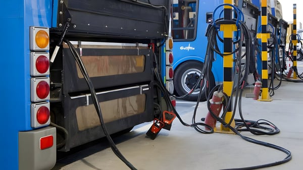Blue EMT Madrid electric buses connected to wired charging cables at a depot station.