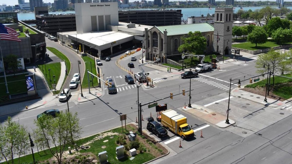 High-angle view of a city intersection with traffic lights, a yellow box truck, and stone buildings near a waterfront.