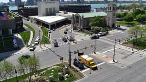 High-angle view of a city intersection with traffic lights, a yellow box truck, and stone buildings near a waterfront.