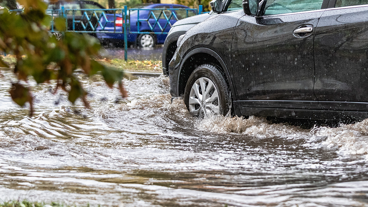 A black SUV driving through a flooded Houston street, splashing muddy water during a heavy rainstorm.