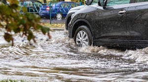 A black SUV driving through a flooded Houston street, splashing muddy water during a heavy rainstorm.