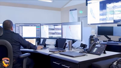 A CAL FIRE operator monitors multiple computer screens displaying maps and data in a wildfire command center.