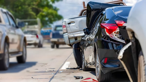 Multi-vehicle rear-end collision involving a black sedan and a silver pickup truck on a multi-lane highway.