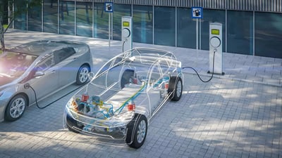 A transparent 3D wireframe of an electric car charging at a sidewalk station next to a silver hatchback.
