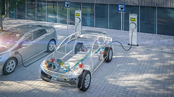 A transparent 3D wireframe of an electric car charging at a sidewalk station next to a silver hatchback.