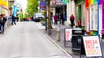 Pedestrians walk along a Reykjavik street featuring a black litter bin positioned between sidewalk cafe signs.