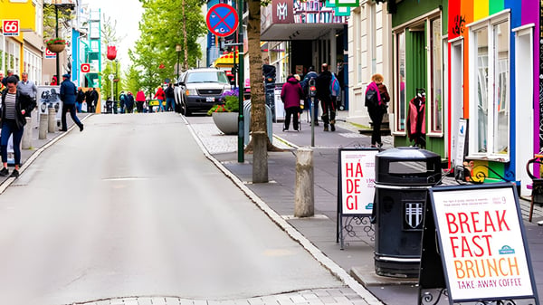 Pedestrians walk along a Reykjavik street featuring a black litter bin positioned between sidewalk cafe signs.