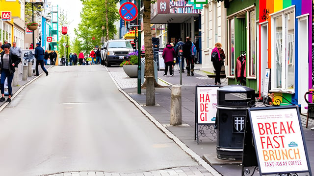 Pedestrians walk along a Reykjavik street featuring a black litter bin positioned between sidewalk cafe signs.