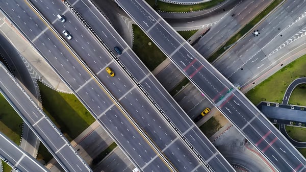 Top-down aerial view of a multi-level highway interchange with cars traveling on asphalt overpasses and ramps.