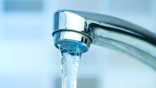 Close-up of a chrome faucet with a steady stream of water flowing against a blurred blue and white background.