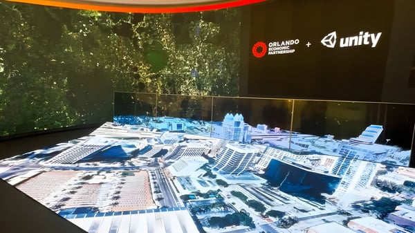 A digital twin of Orlando projected on a table with Orlando Economic Partnership and Unity logos on a screen behind it.