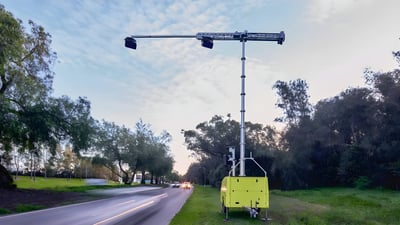 Mobile Acusensus AI camera trailer deployed on a grassy roadside to monitor traffic on a two-lane highway.
