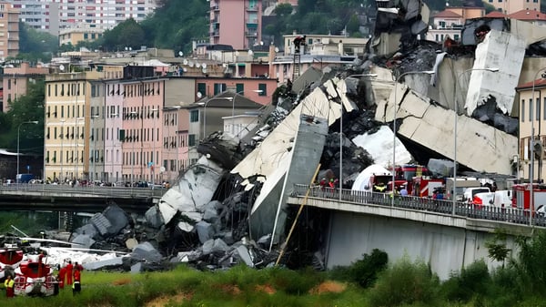 Collapsed concrete bridge sections and rubble in an urban area with emergency vehicles and first responders present.