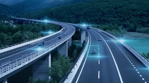 Elevated highway curves through a forested valley with digital blue light overlays on vehicles and infrastructure
