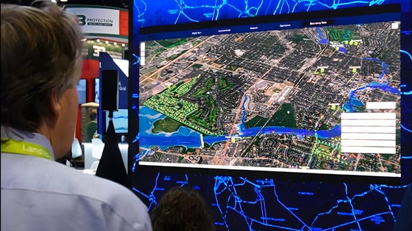 A person at a trade show viewing a Landis+Gyr digital map display of a city grid with utility data overlays.