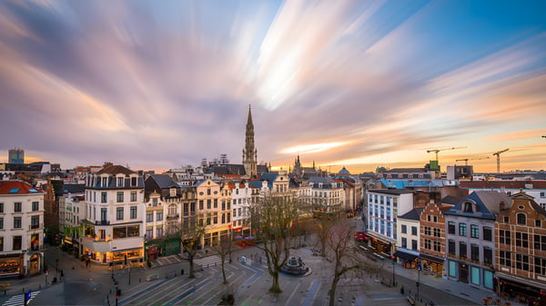 Elevated view of Brussels city center at sunset featuring historic architecture, the Town Hall spire, and a public square.