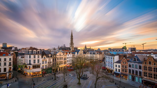 Elevated view of Brussels city center at sunset featuring historic architecture, the Town Hall spire, and a public square.