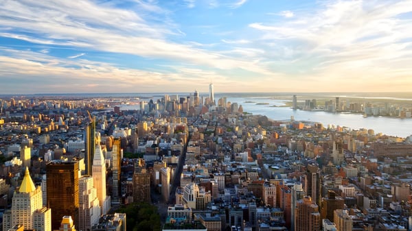 Aerial view of the Manhattan skyline and Hudson River in New York City under a bright sky with wispy clouds.
