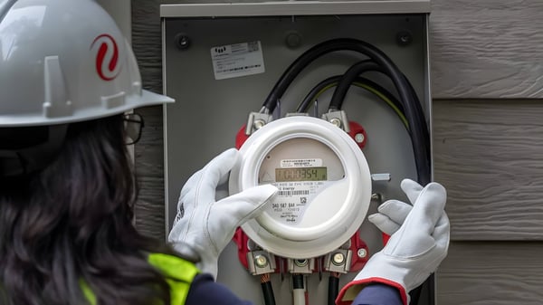 A technician in a white hard hat and gloves installs a digital electric smart meter into an outdoor residential utility box.