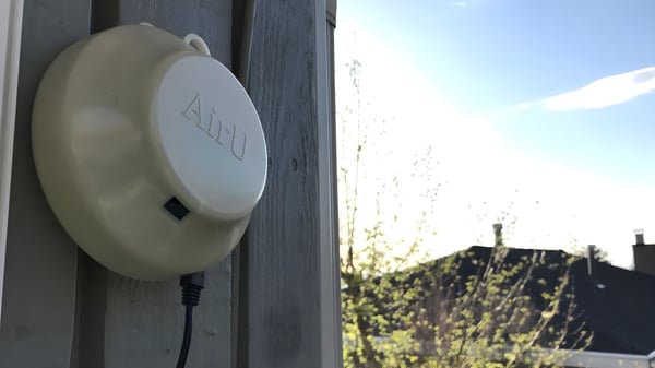 An AirU air quality sensor mounted to a wooden exterior wall overlooking a residential neighborhood.