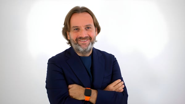 Portrait of Gianluca Longo wearing a navy blazer and an orange smartwatch against a white background.