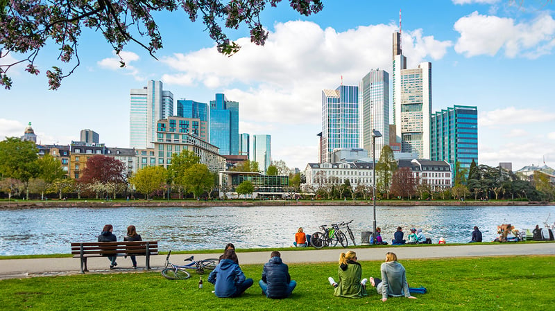 A picturesque scene of individuals sitting on a park bench near a river in a green smart city