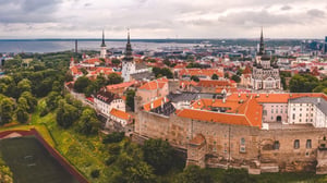 Aerial panoramic view of Tallinn's Old Town with historic buildings, spires, red roofs, a stadium, and a harbor in the distance.