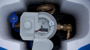 Close-up of a smart water meter with brass fittings installed inside a protective white foam casing