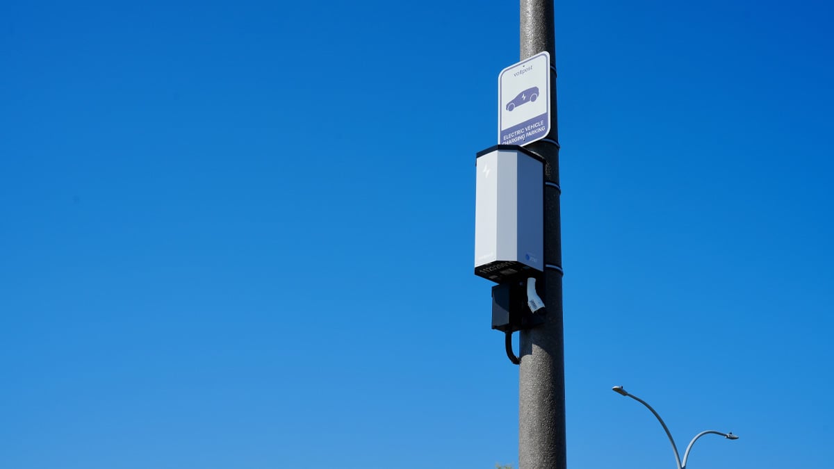 Voltpost EV charger unit mounted on a gray lamppost against a clear blue sky, with a small sign above it.