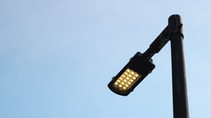 Close-up of a modern LED street light fixture with multiple yellow-glowing diodes against a clear blue sky.