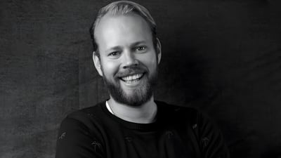 Black and white headshot of a smiling man with a beard wearing a dark sweater against a textured background.