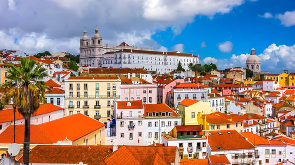 Lisbon cityscape featuring red-tiled roofs, colorful buildings, and the Monastery of São Vicente de Fora under a blue sky.