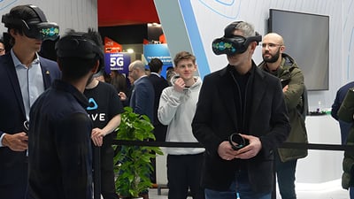 Attendees wearing VR headsets and holding controllers at a crowded technology exhibition with 5G signage.