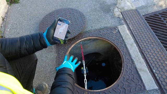 A man inspecting an IoT smart gutter device with a portable device