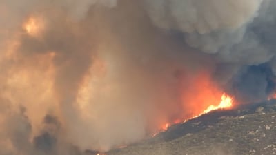Thick plumes of orange and grey smoke rising from a wildfire burning across a hillside.