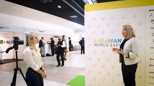 Donna Moore being interviewed on camera in front of a LoRaWAN World Expo backdrop at a convention center.