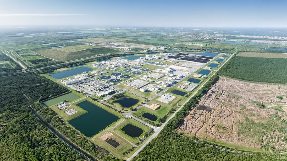 Aerial view of a large water treatment facility with circular clarifiers and retention ponds surrounded by green fields
