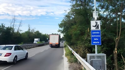 Traffic on a Milan highway passing an electronic speed control sign and roadside monitoring equipment.