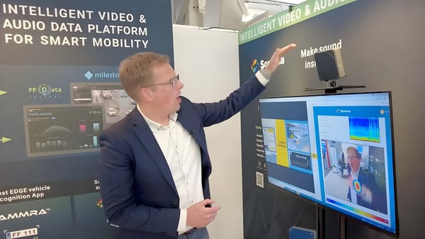A man in a suit gestures toward a sensor and monitor at a Samiraa smart mobility data platform exhibition booth.