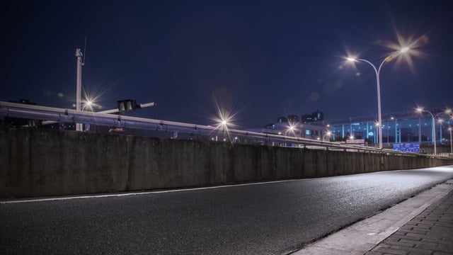 Lit street lamps with starburst glare along a concrete road barrier and empty asphalt road at night under a dark blue sky