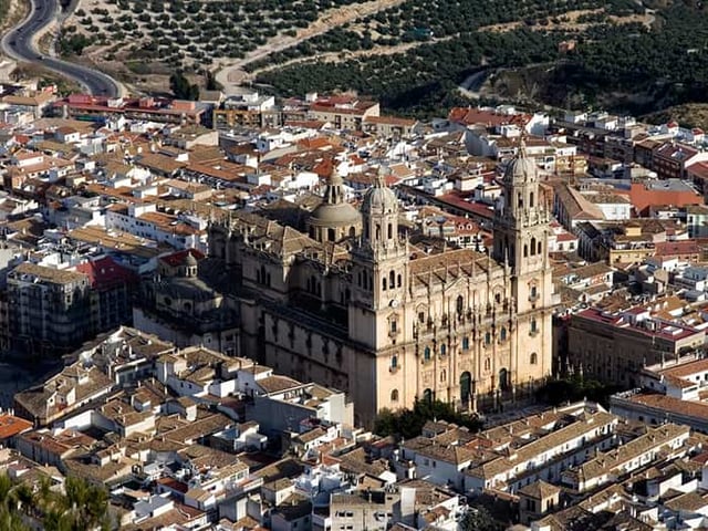 Aerial view of the Jaén Cathedral surrounded by dense urban housing and olive groves in Spain.