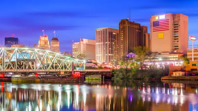 Newark skyline at dusk featuring the Bridge Street Bridge and illuminated office buildings reflecting on the Passaic River.